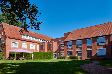 Blick auf den Garten der St. Anna Klinik Löningen, mit Terrasse und dem Gebäude der Klinik im Hintergrund